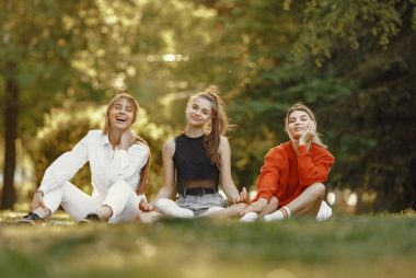 Three friends sitting on grass, enjoying a sunny outdoor day in the park.