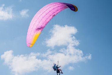 Experience the thrill of tandem paragliding with colorful parachute soaring high in the clear blue sky.
