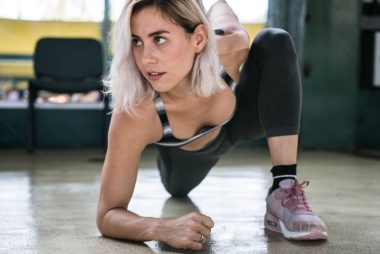 Focused woman with blond hair stretching indoors, showcasing determination and fitness.